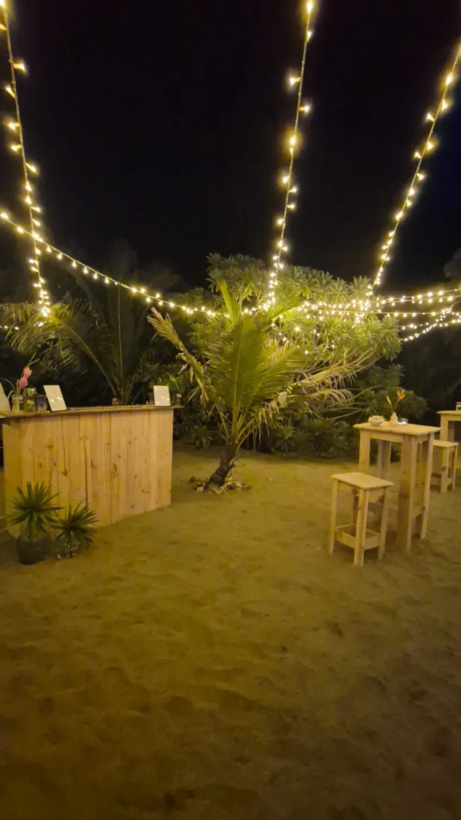 Bar en bois, mange-debout et guirlandes lumineuses installés pour une soirée en extérieur à La Réunion