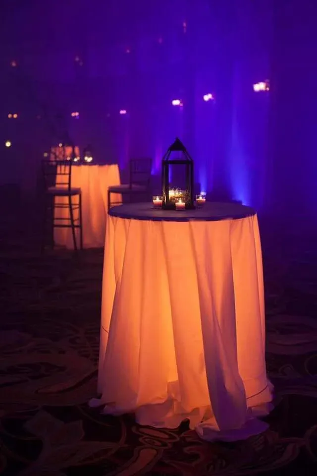 Mange-debout habillé d'une nappe éclairée de l'intérieur, avec une lanterne noire et des bougies, dans une salle plongée dans une lumière violette