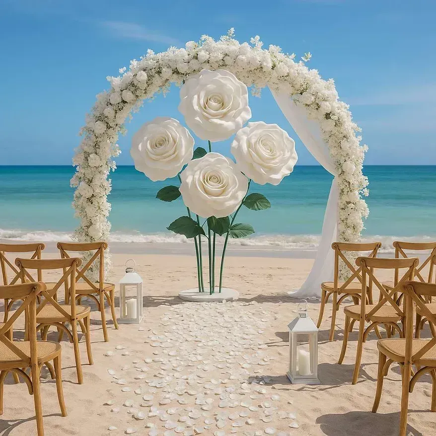 Arche ronde fleurie de blanc sur une plage, avec de grandes roses blanches et des chaises en bois