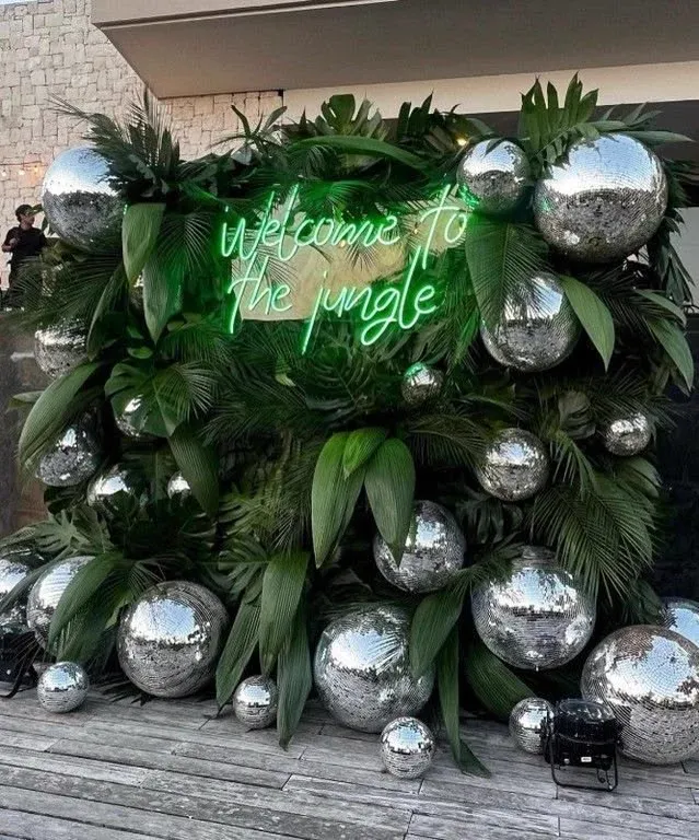 Mur de feuillages et de boules miroir avec un néon vert