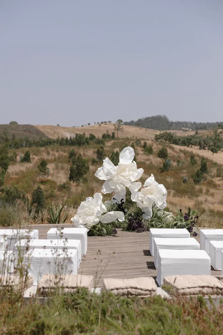 Cérémonie de mariage en extérieur : bancs blancs face à une composition de fleurs blanches, sur une colline